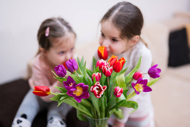 Two sisters with spring tulip bouquet.  Holiday decor with flowers colorful tulips.  - Fotografie, Obrázek