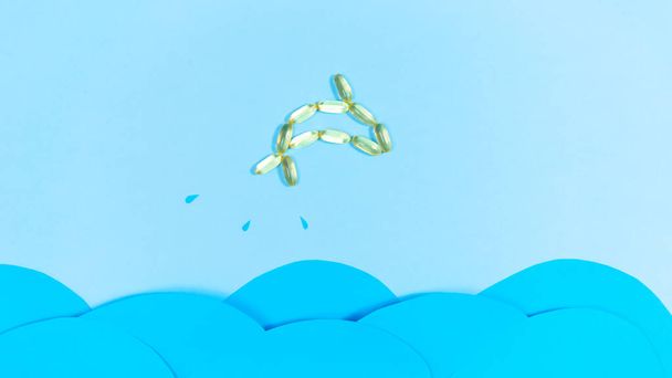 Peixe feito de cápsulas amarelas transparentes com óleo de peixe, Omega 3, salta para fora do mar acima das ondas azuis. Manutenção e melhoria da saúde. - Foto, Imagem