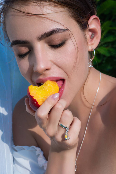 Country woman. Stylish sensual woman posing on summer greenery outdoor. Woman eat peach, close up. Country girl with peach close up. Close up woman face eating peach in nature - Photo, Image