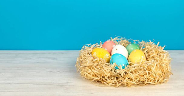 Painted Easter eggs in a nest on a blue background. Place for text. The concept of Easter holidays - Foto, Imagem