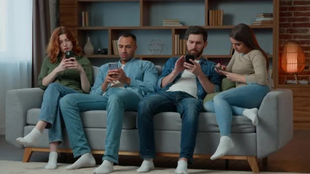 Grupo amigos gente de negocios se sientan en el sofá con teléfonos móviles charlando en las redes sociales ignorándose entre sí mujeres y hombres adictos multiétnicos utilizan diversos dispositivos de adicción a la tecnología moderna gadgets abuso - Metraje, vídeo