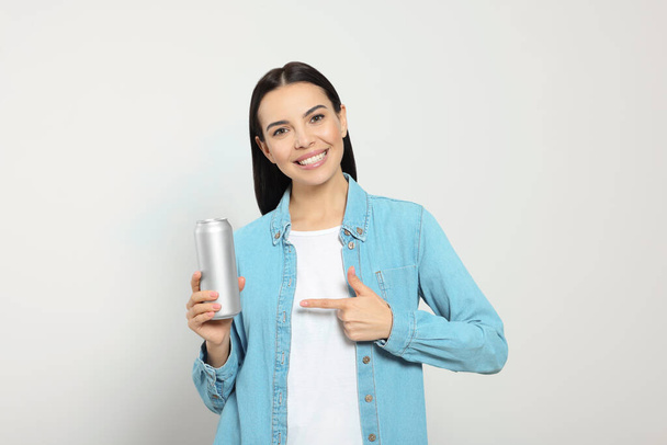 Beautiful happy woman holding beverage can on light grey background - Photo, image