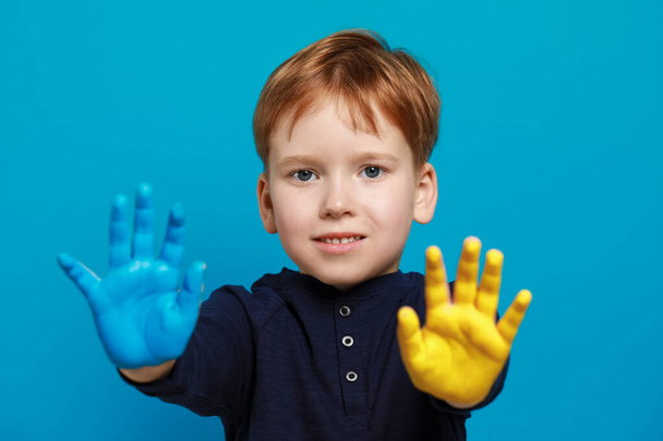 Little boy with hands painted in Ukrainian flag colors on light blue background. Love Ukraine concept - 写真・画像