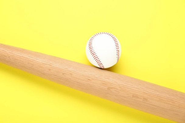 Houten honkbalknuppel en bal op gele achtergrond, plat gelegd. Sportuitrusting - Foto, afbeelding