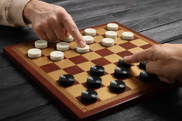 Man playing checkers with partner at black wooden table, closeup - Foto, Bild