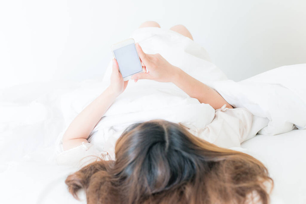 Asiatin liegt auf dem Bett und benutzt ihr Smartphone. Konzeptionelle Aufnahme einer Frau beim Telefonieren. - Foto, Bild