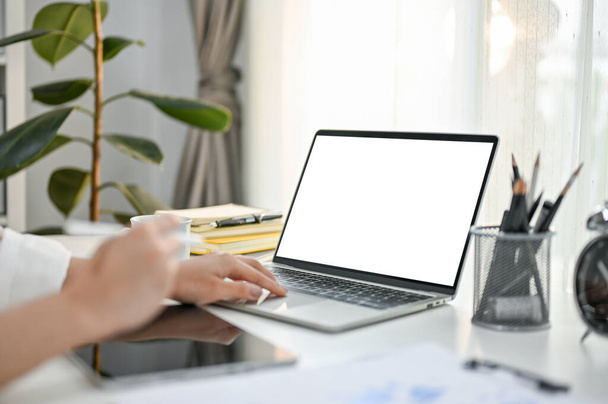 Close-up side view beeld van een zakenvrouw met behulp van haar laptop aan haar bureau in modern helder kantoor. laptop blanco scherm mockup voor het weergeven van uw grafische advertenties. - Foto, afbeelding
