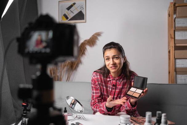 Mulher blogueira de beleza filmando tutorial de maquiagem na câmera em estúdio em casa. Influenciador menina transmissão ao vivo cosméticos revisão do produto. Feminino vlogger mostrando paleta de sombra. Espaço de cópia - Foto, Imagem