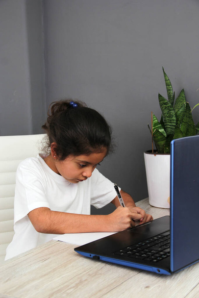 9-year-old Latino girl does home schooling takes online classes at home on a desk with a laptop, studies, is surprised and participates in class - Φωτογραφία, εικόνα