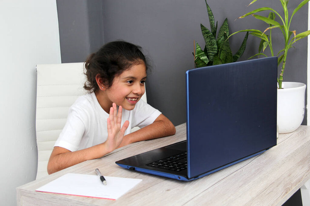 9-летняя латиноамериканка занимается домашним обучением берет уроки дома на рабочем столе с ноутбуком, учится, удивляется и участвует в занятиях - Фото, изображение