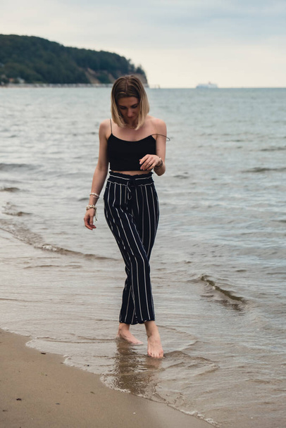 Young woman standing on blurred beachside background. Attractive female enjoying walking the sea shore. travel and active lifestyle concept. Springtime. Relaxation, youth, love, lifestyle solitude - Photo, Image