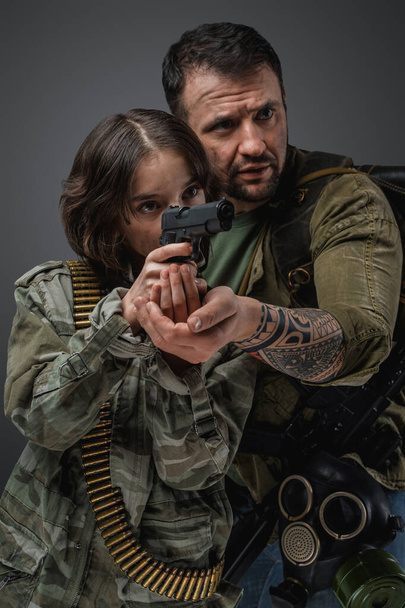 Portrait of post apocalyptic man teaching little girl to shoot in setting of post apocalypse. - Фото, изображение