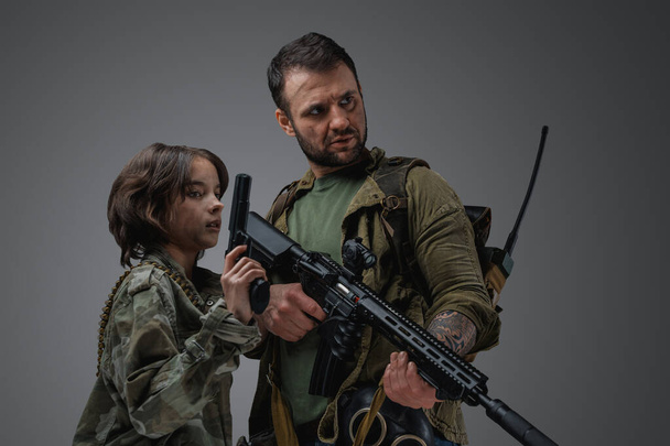 Studio shot of post apocalyptic military man protecting young girl against gray background. - Foto, Imagem