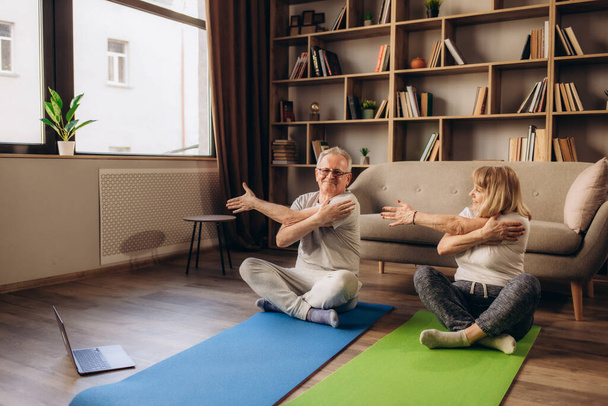 Feliz anciana de mediana edad de 50 años pareja aprendiendo a meditar en casa viendo en vivo clases de yoga en la televisión en línea tutorial en el sitio web mirando el ordenador portátil haciendo ejercicios de entrenamiento virtual de fitness. - Foto, Imagen