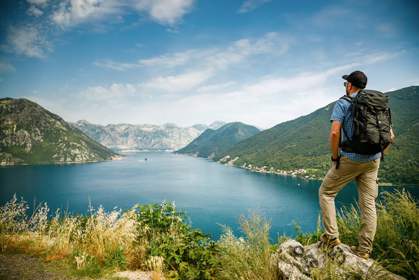 Tourist man standing on the edge of a cliff, enjoying amazing sea view of the Bay of Kotor, Montenegro - Fotoğraf, Görsel