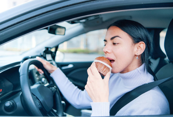 Jedna kobieta prowadzi samochód i je jedzenie za kierownicą. - Zdjęcie, obraz