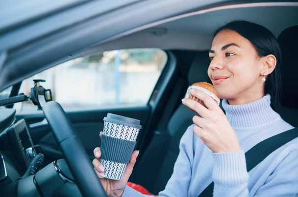 Une femme conduisant une voiture et prenant le petit déjeuner - Photo, image