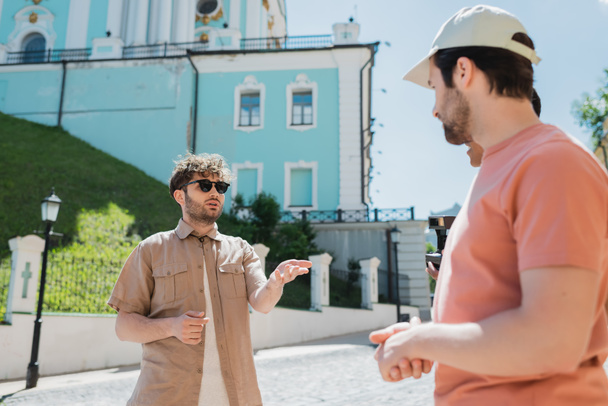 junger Reiseleiter mit Sonnenbrille im Gespräch mit multiethnischen Touristen auf der Andreasabfahrt in Kiew - Foto, Bild