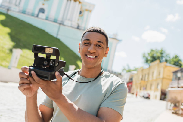 carefree african american tourist with vintage camera smiling on Andrews descent in Kyiv - Φωτογραφία, εικόνα
