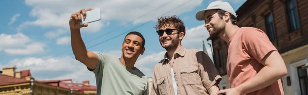 happy african american traveler taking selfie with tour guide in sunglasses and bearded man on Andrews descent in Kyiv, banner - Fotoğraf, Görsel