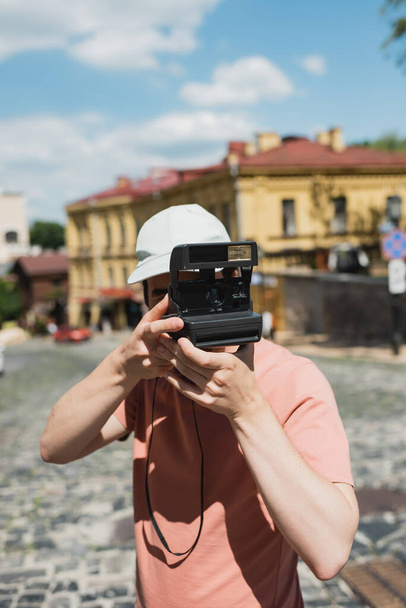 Молодий чоловік у сонячній шапці фотографує вінтажний фотоапарат на спуску Ендрюса у Києві. - Фото, зображення