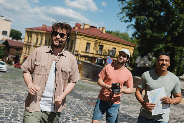 turistas multiétnicos positivos com câmera vintage e mapa sorrindo durante a excursão com guia turístico em descida Andrews em Kiev - Foto, Imagem