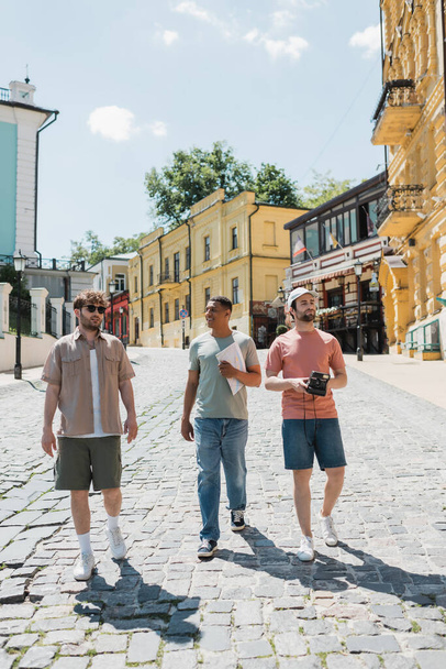 Çok ırklı turistler harita ve klasik kamerayla Andrews kaldırımında Kyiv 'e doğru yürüyorlar. - Fotoğraf, Görsel
