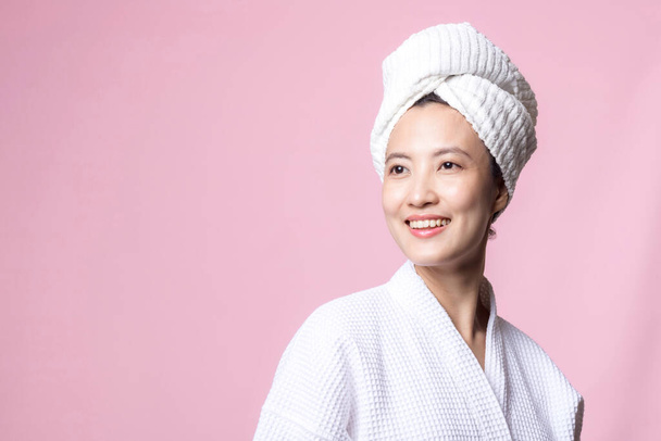 mooie jonge Aziatische vrouw blij met schone gezichtshuid in handdoek en badjas, spa pak op roze achtergrond. Huidverzorging, behandeling, wellnesstherapie, gezichtsverzorging, schoonheidsverzorging voor vrouwen, kosmetologisch concept - Foto, afbeelding