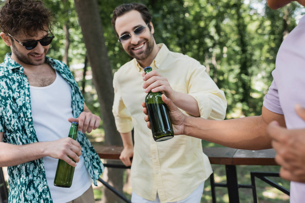 beztroskie i stylowe międzyrasowych przyjaciół trzymających butelki świeżego piwa w parku letnim - Zdjęcie, obraz