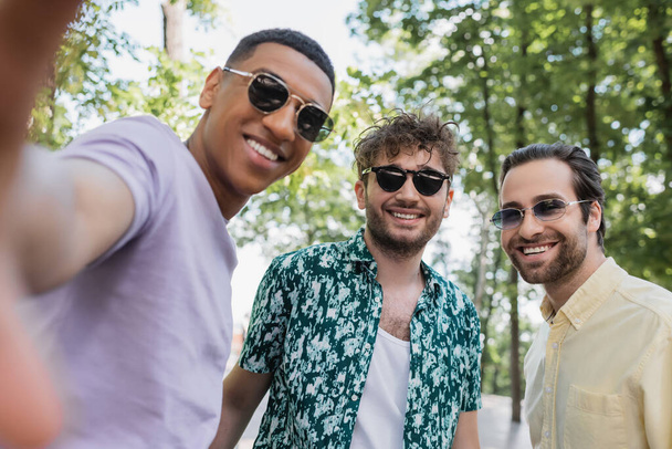 Fröhliche multiethnische Freunde mit Sonnenbrille stehen im Sommer im Park  - Foto, Bild