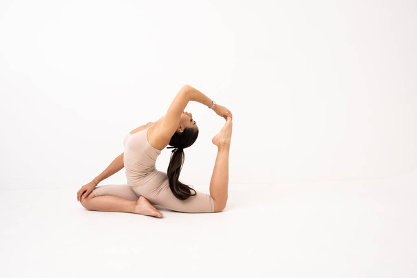 Girl doing stretching in the studio on a white background. A beautiful gymnast with a flexible body and athletic uniform. - Foto, Imagen