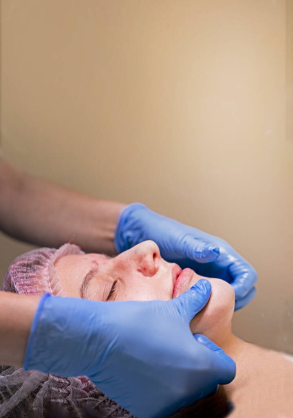 primer plano haciendo masaje facial con aceites esenciales a una adolescente en un salón de spa. vertical - Foto, imagen
