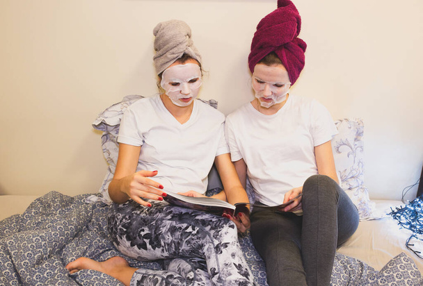 Girls in skin mask sheet on face. Beauty procedures at home. Hen party. Women reading magazine. - Foto, Imagen