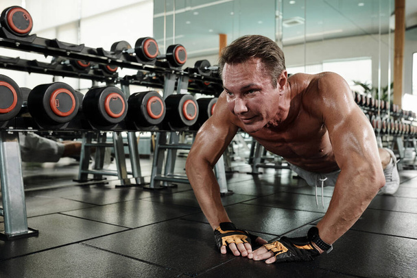 Fit mature man doing diamond push-ups on gym floor - Photo, image