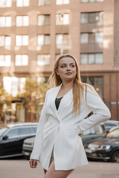 Blond stylish woman at oversized white jacket posing at the city background - Photo, Image