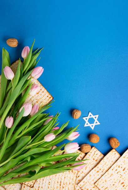 Jewish holiday Passover greeting card concept with matzah, nuts, tulip flowers on blue table. Seder Pesach spring holiday background, top view, copy space. - Photo, Image