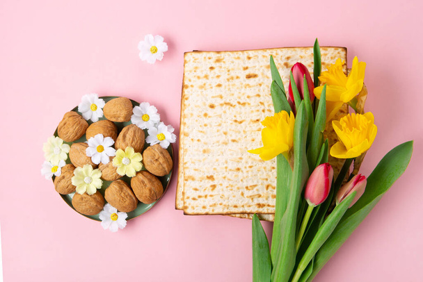 Jewish holiday Passover greeting card concept with matzah, Star of David, spring yellow daffodil, tulips, daisy flowers, walnuts on pink table. Seder Pesach spring holiday background, copy space. - Photo, Image
