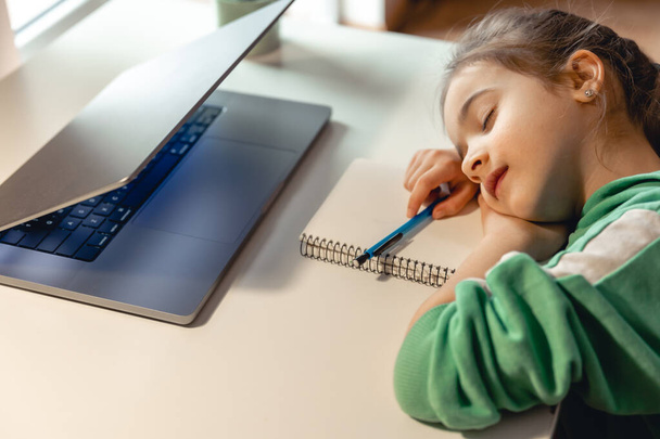 Маленькая девочка спит перед ноутбуком на столе, уставший ребенок заснул во время уроков. - Фото, изображение