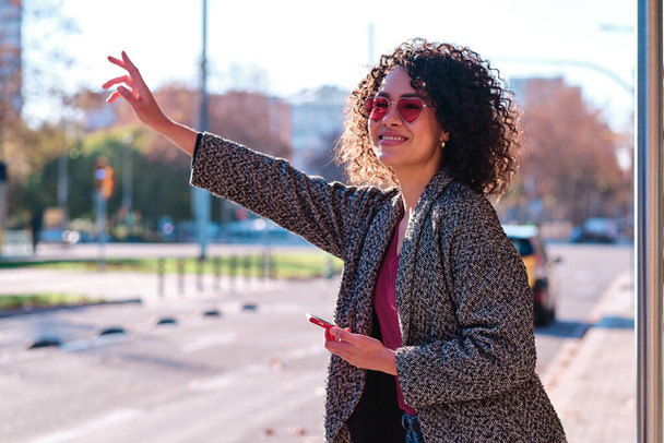 Egy nőre fókuszáló portré, aki felemeli a kezét, hogy taxit hívjon a városban. - Fotó, kép