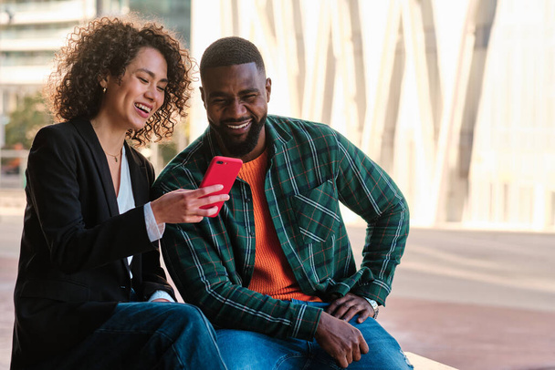Muotokuva onnellisia afrikkalaisia ystäviä käyttäen mobiili istuu kadulla - Valokuva, kuva