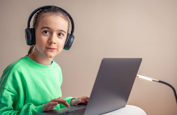 Funny little girl in headphones with laptop plays games, game addiction concept, copy space. - Фото, зображення
