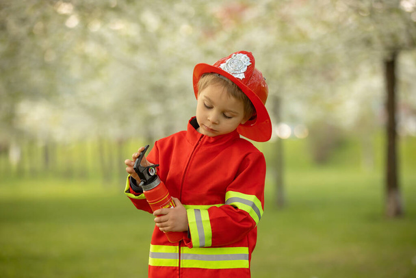 Little toddler child with fireman costume in park, pretending to be real fireman, playing on sunset - Fotoğraf, Görsel