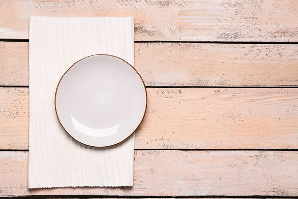 Empty plate and folded napkin on light wooden background - Fotó, kép