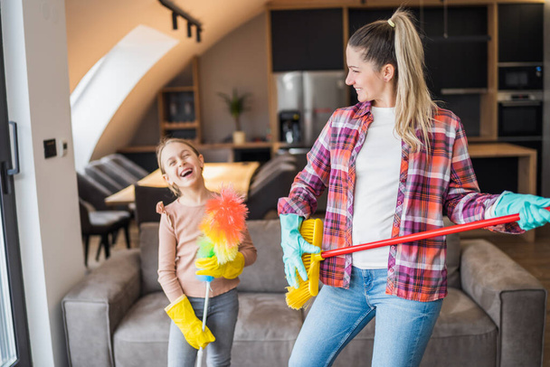 Feliz madre e hija divirtiéndose mientras limpian la casa juntas. - Foto, imagen