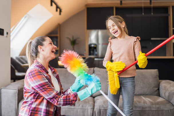 Happy mother and daughter having fun while cleaning  house together. - Foto, imagen