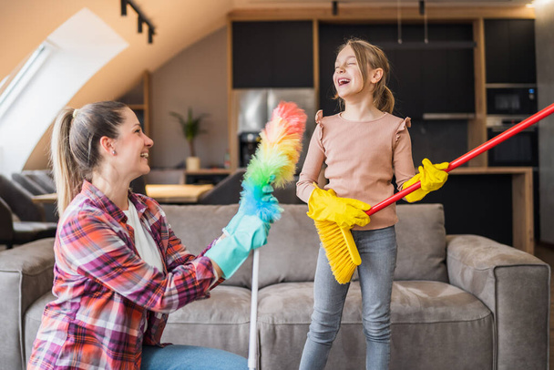 Happy mother and daughter having fun while cleaning  house together. - Foto, afbeelding