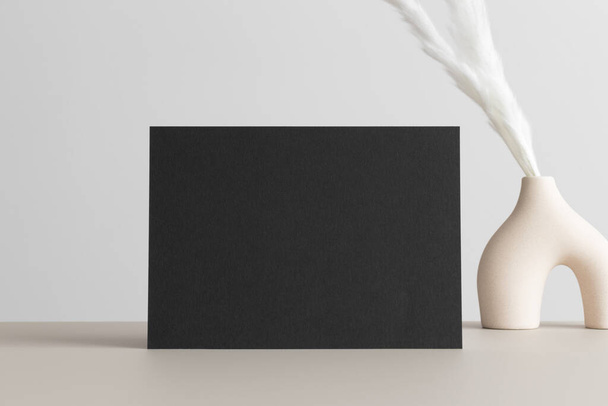 Чорний макет запрошень з прикрасою брошур на бежевому столі. 5x7 співвідношення, подібне до A6, A5
. - Фото, зображення