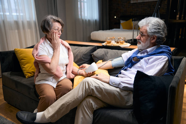 Ηλικιωμένη γυναίκα μετρά την αρτηριακή πίεση του συζύγου της με τονόμετρο, ανησυχεί για την κατάστασή του - Φωτογραφία, εικόνα