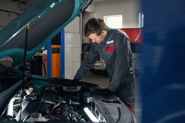 Mechanic in protective clothes standing near car with open hood and change parts in tire fitting. - Foto, Imagen