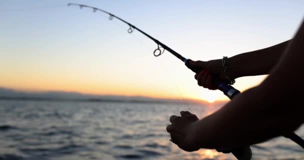 Touriste personne tient tige de filature dans les mains et capture des poissons dans la mer. Pêche au coucher du soleil en soirée - Séquence, vidéo